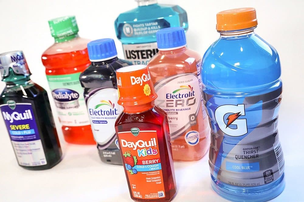 Bottles of brightly dyed drinks and medicines (NyQuil, Gatorade, DayQuil) on a white seamless, bright high-key light