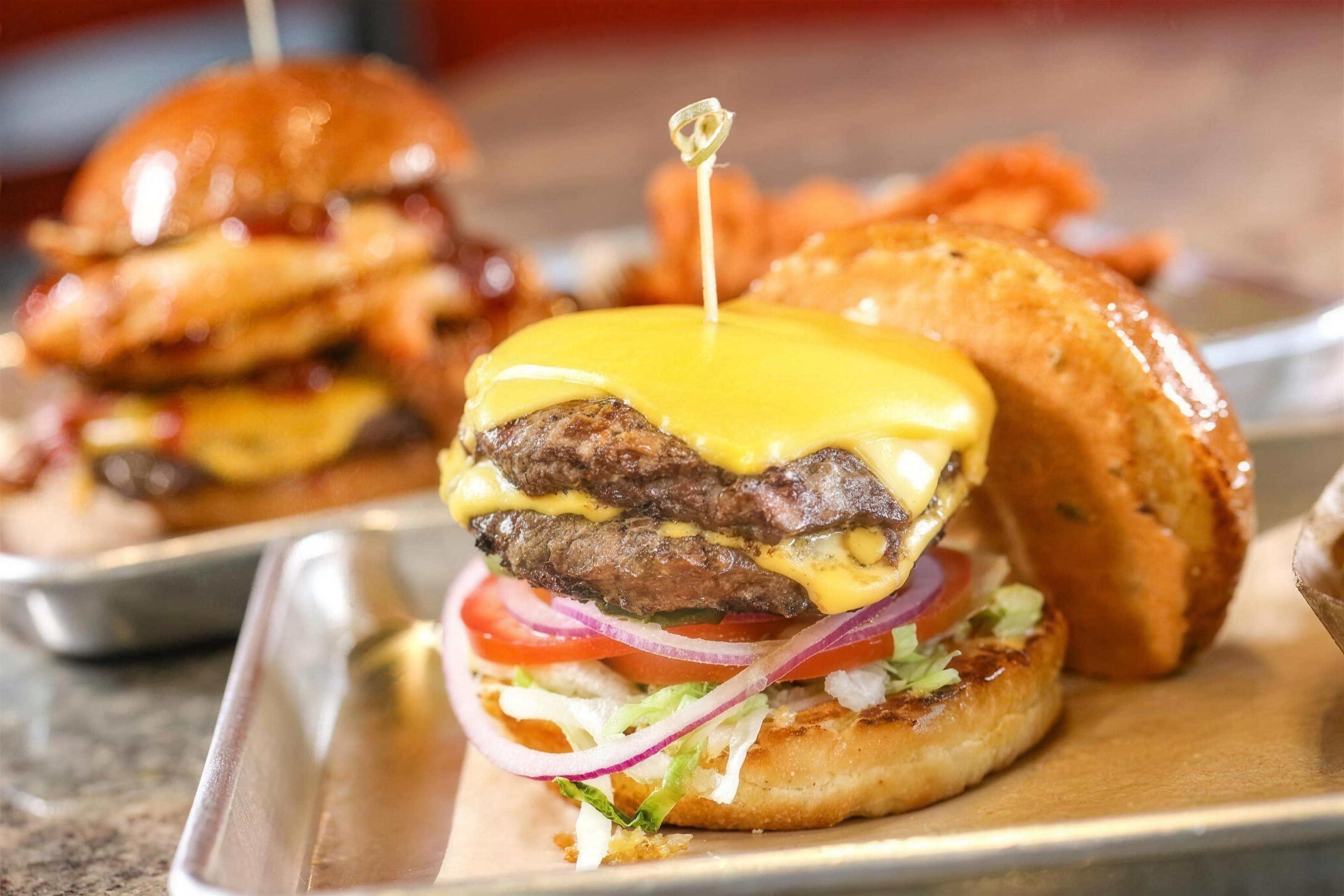 Double cheeseburger with melted American cheese on a metal tray, onion rings behind, warm dark background