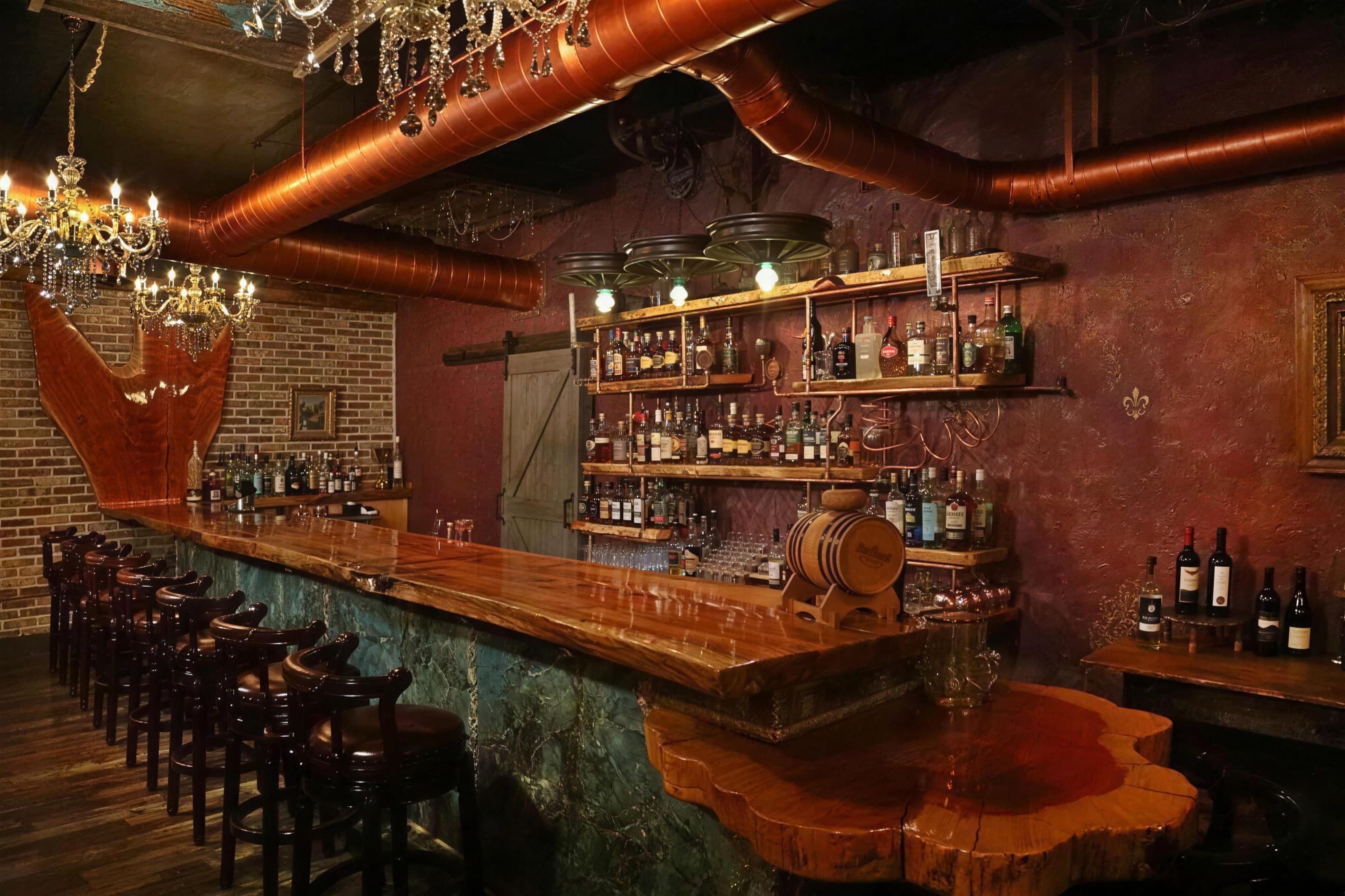 C&C Social Club bar with live-edge counter, copper ceiling and backlit shelves, warm low light