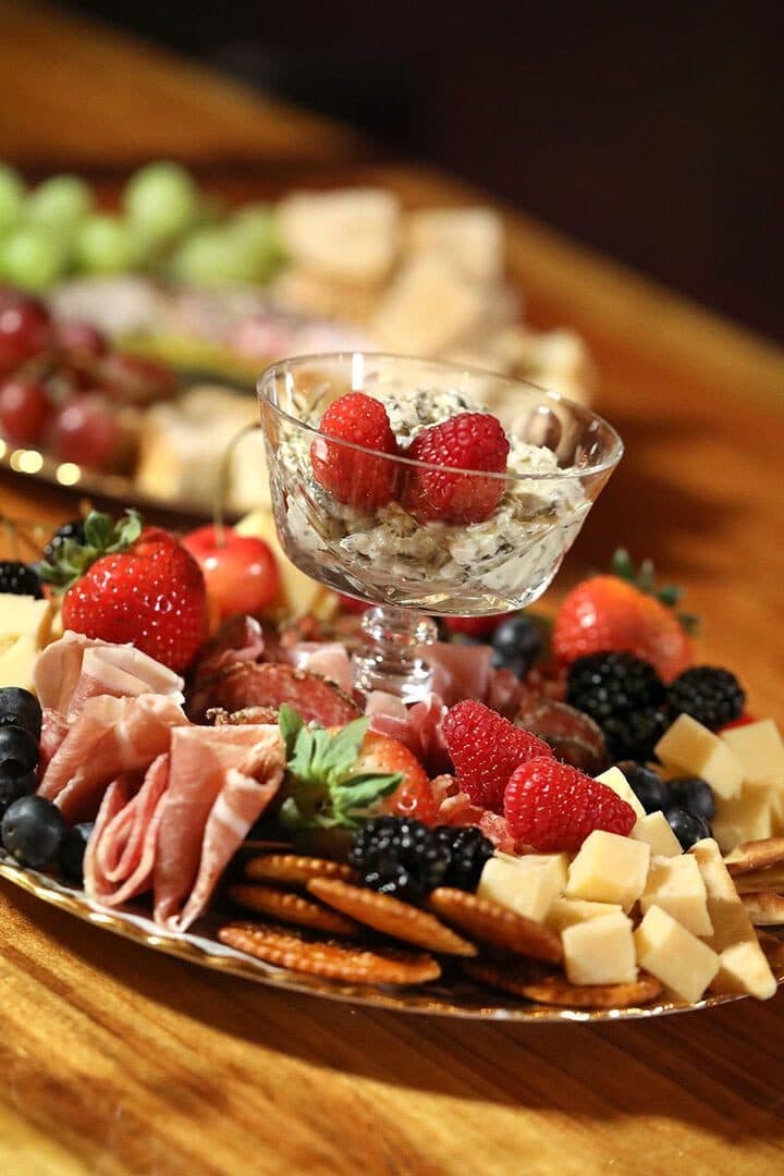 Charcuterie platter with strawberries, cheeses and a parfait glass, shallow depth of field, dark warm background
