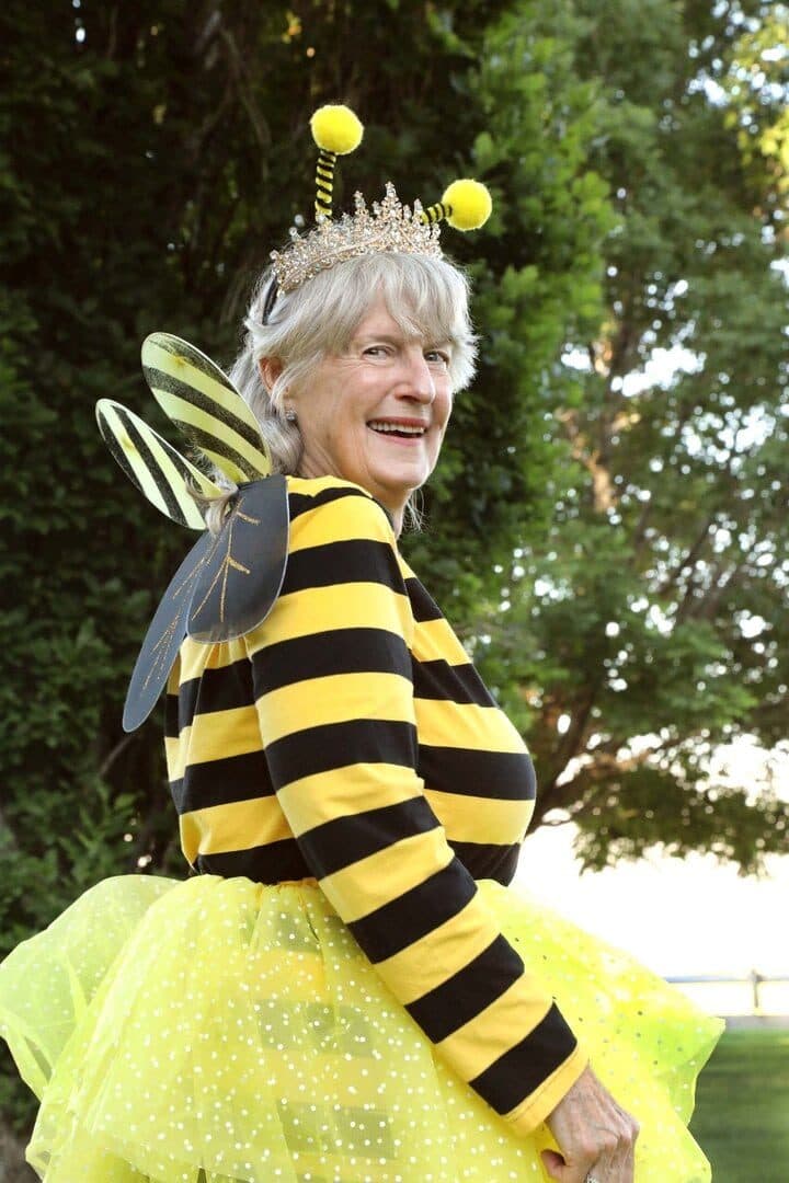 Master gardener in a bee costume with antennae and wings, smiling outdoors in green garden light