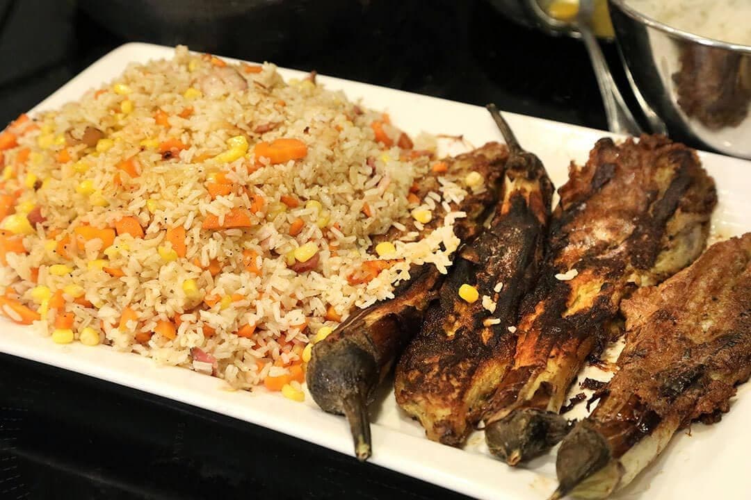 Platter of fried rice with carrots next to roasted Chinese eggplant, white platter, dark background