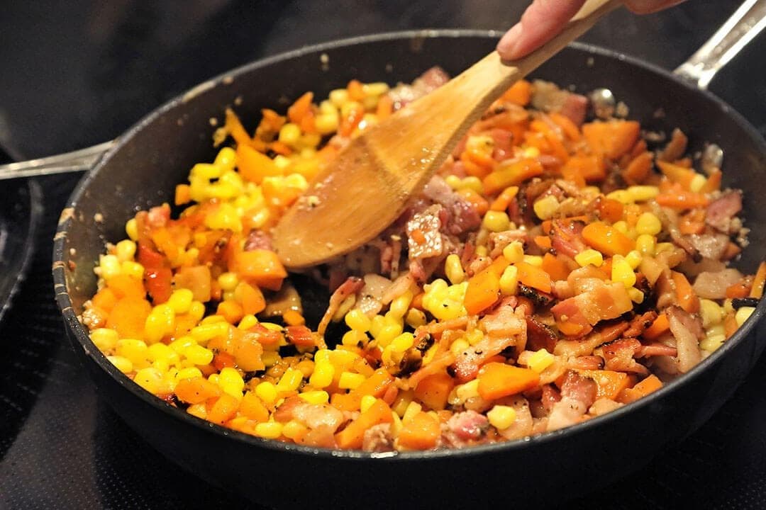 Wooden spoon stirring fried rice with corn and carrots in a black skillet, top-down warm light