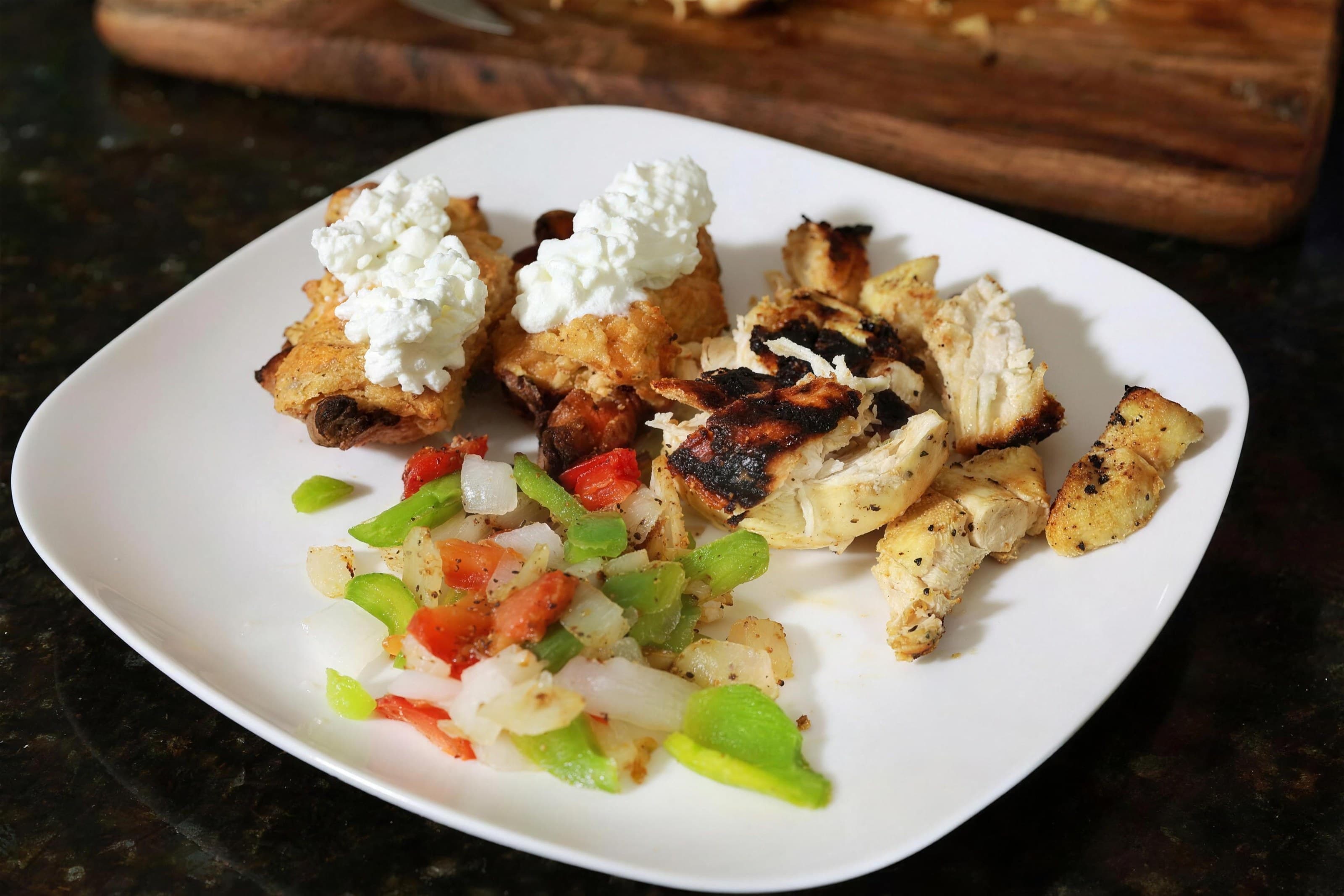 White plate of grilled chicken, cottage cheese and diced pepper salad, dark counter