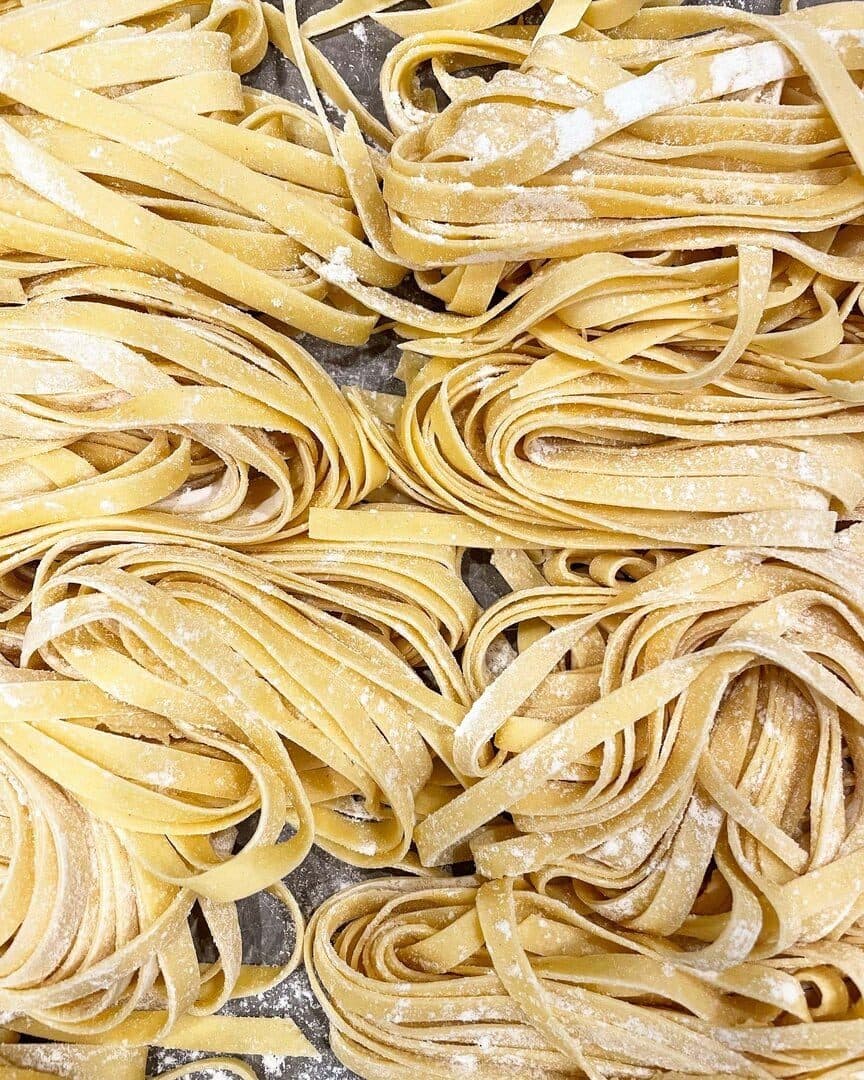 Nests of fresh fettuccine dusted with flour, top-down, warm tones