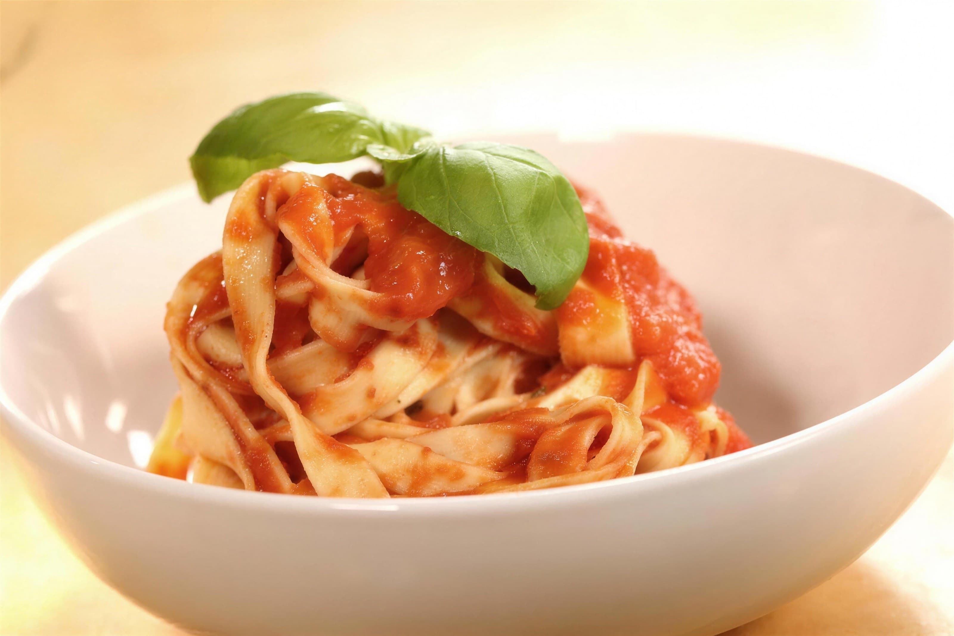Tagliatelle in marinara with a basil sprig in a white bowl, bright high-key light