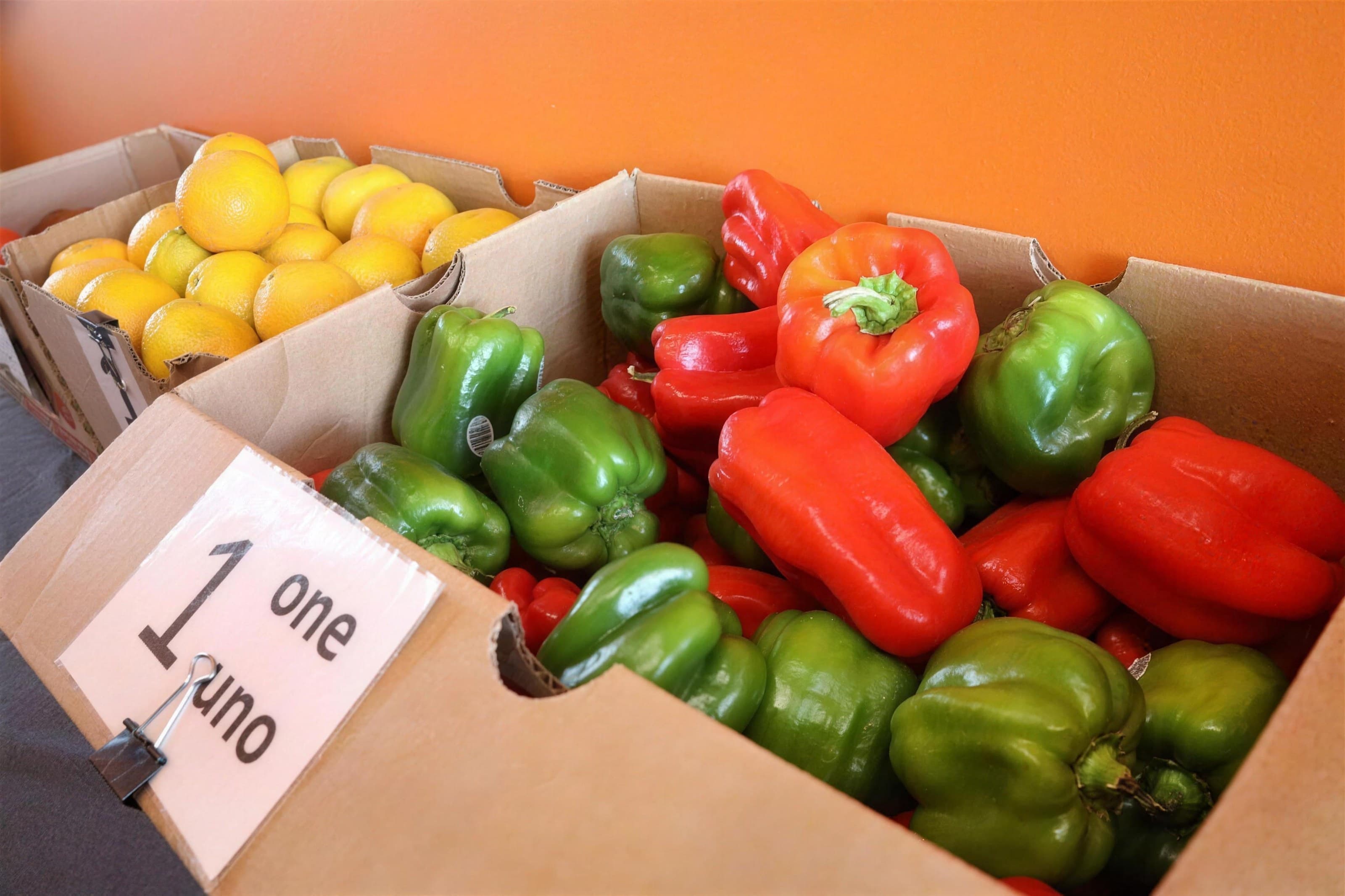 Boxes of red and green bell peppers and lemons in a food pantry, orange wall