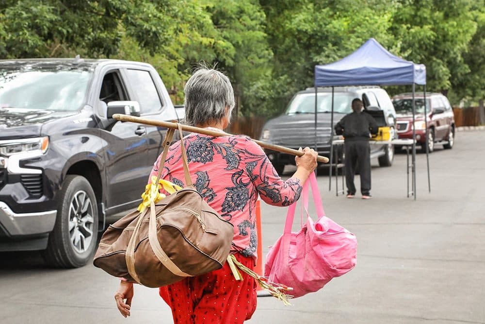 Woman carrying produce bags on a pole across a parking lot at a mobile food distribution