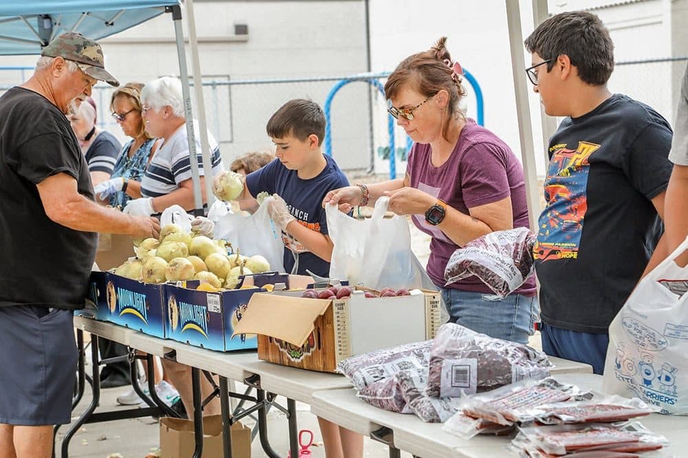 Volunteers handing out produce and bags at folding tables at a church mobile harvest