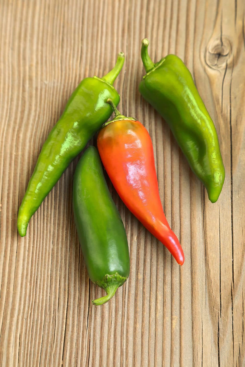 Three green Anaheim peppers and one red pepper on weathered wood, top-down, natural light