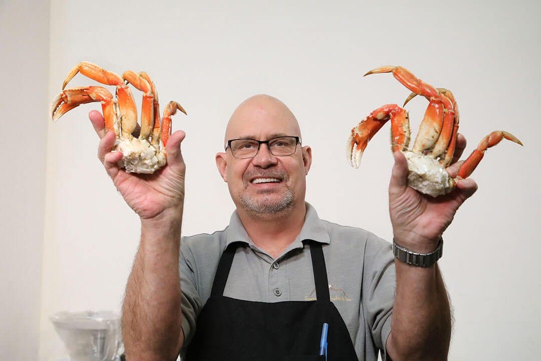 Seafood manager holding up two Dungeness crab clusters against a white wall