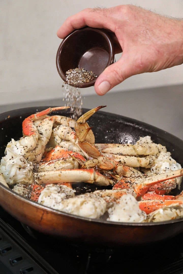 Hand sprinkling Szechuan pepper over sautéed Dungeness crab in a skillet, dark background