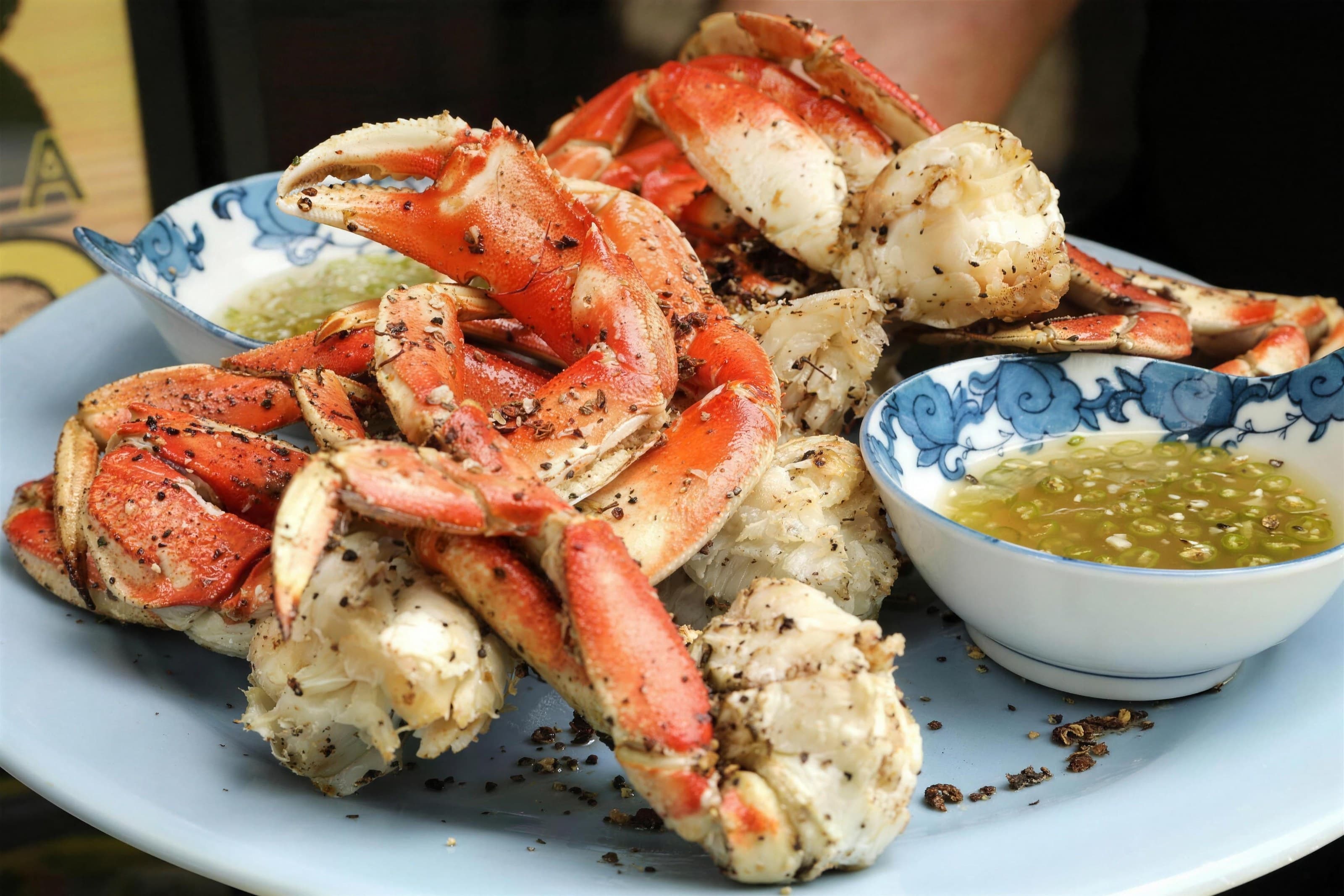 Pepper-crusted Dungeness crab legs on a blue plate with garlic butter dipping bowls