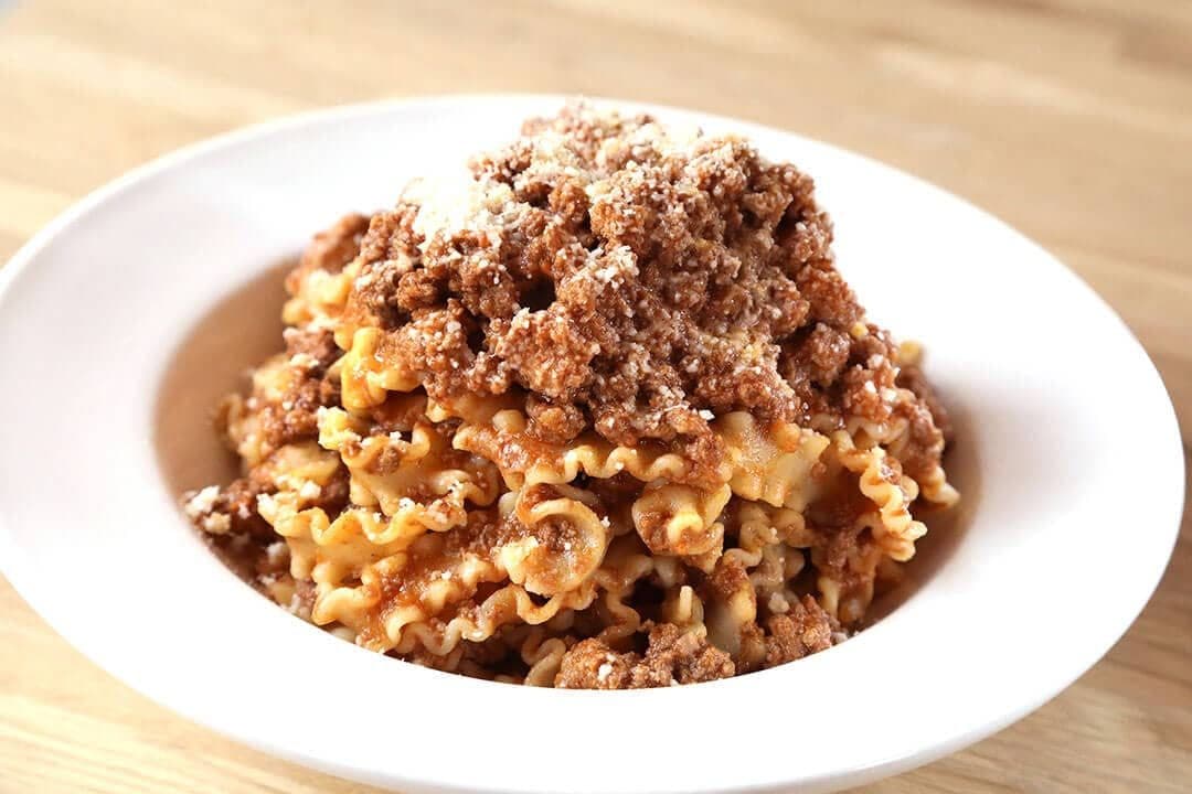 Mafaldine noodles with meat Bolognese and grated cheese in a white bowl, wooden table