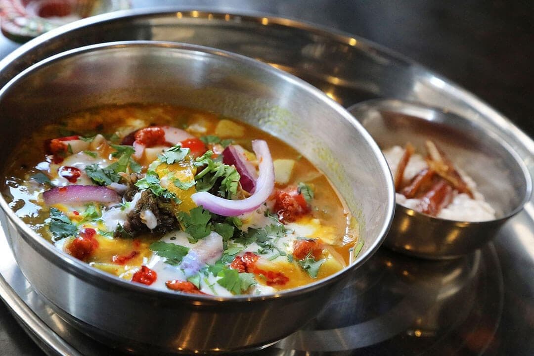 Steel bowl of sweet potato and bell pepper curry with onion and cilantro, dark background