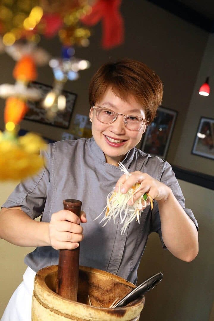Chef holding green papaya shreds over a wooden mortar, colorful restaurant behind