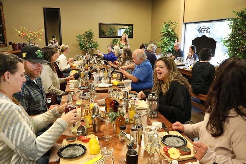 Long table of class participants mixing cocktails at a distillery, warm interior