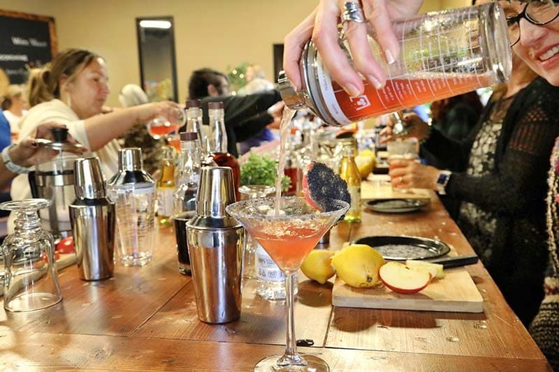 Pouring a red cocktail from a shaker into a martini glass over a table of bar tools