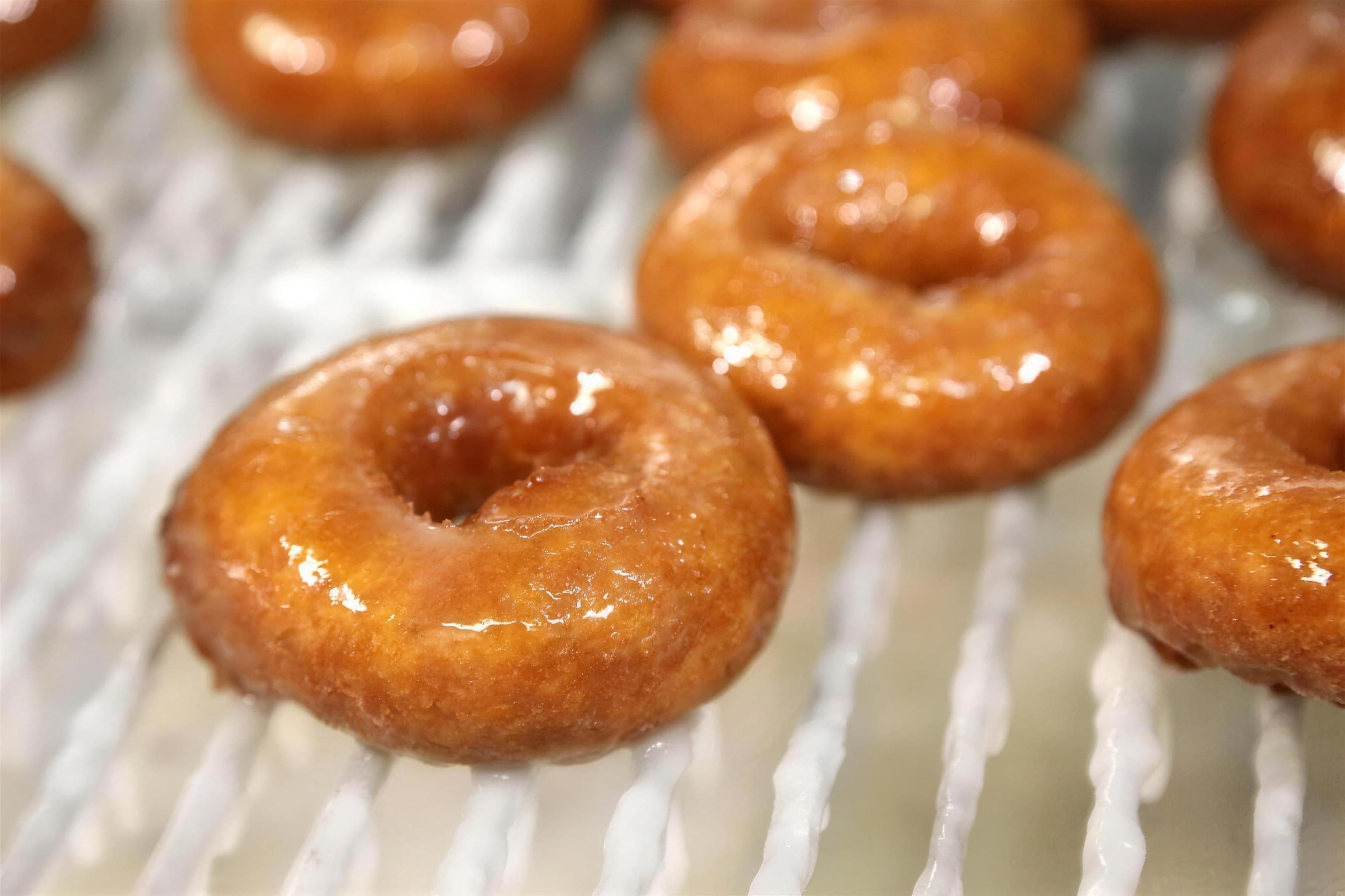 Glazed pumpkin doughnuts on a cooling rack, glossy close-up, high-key light