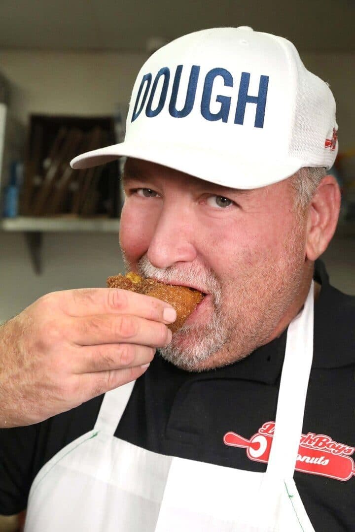 DoughBoys owner in a DOUGH cap biting into a pumpkin doughnut
