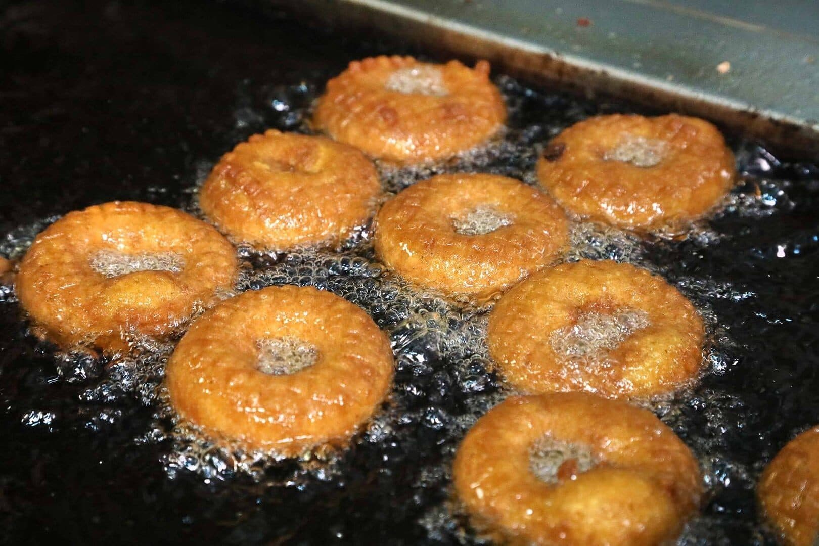 Pumpkin doughnuts frying in bubbling oil, top-down, dark