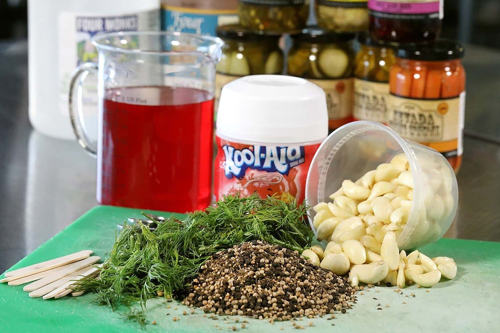 Cherry Kool-Aid, pickle jars, dill, garlic and peppercorns on a green board