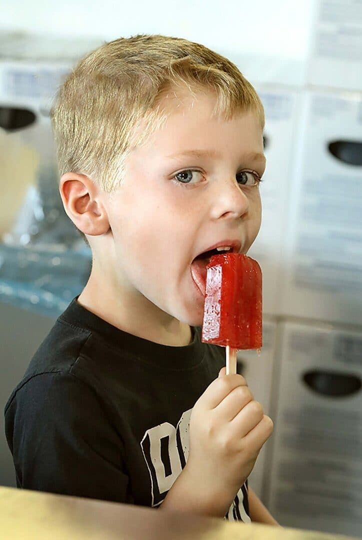 Young boy licking a red pickle-juice popsicle, close-up, white background