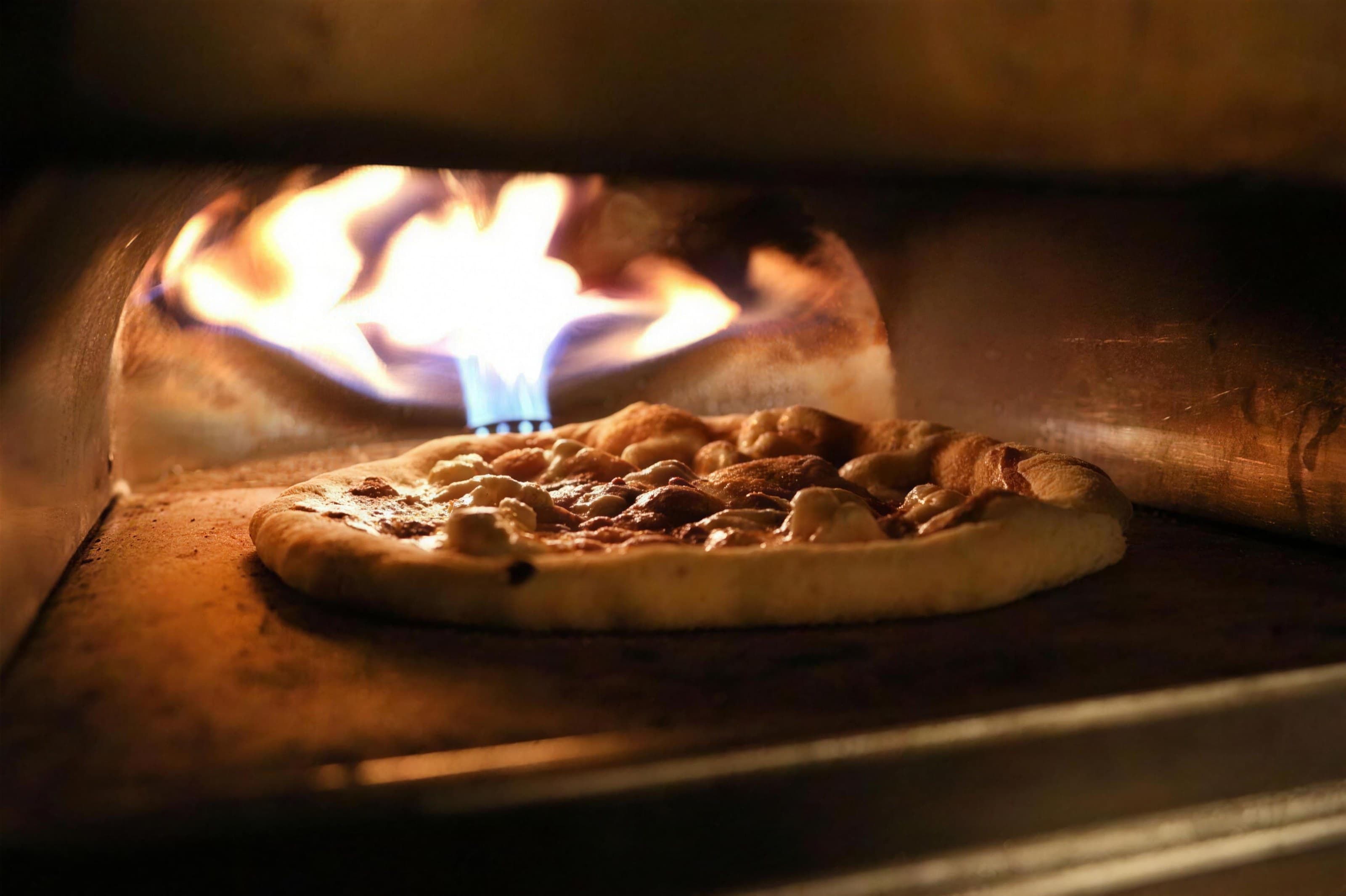 Sourdough pizza baking in a wood-fired oven with flame, dark warm
