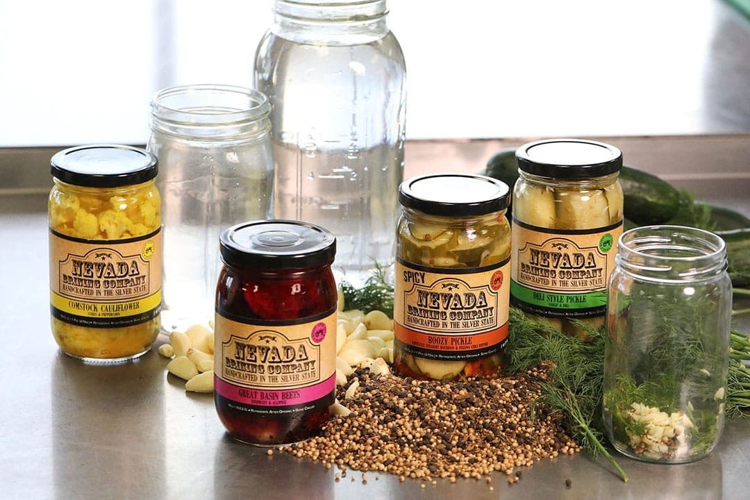 Nevada Brining Co. pickle jars with spices, garlic and dill on a steel counter, bright