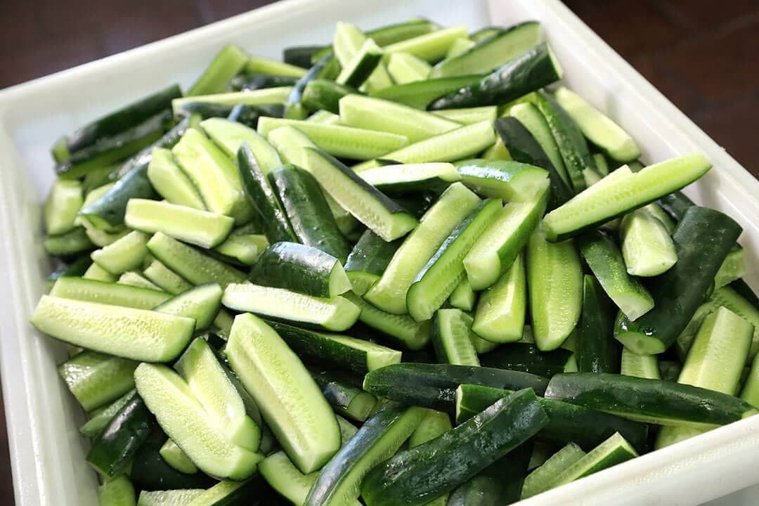 Tray of hand-cut cucumber spears, top-down, fresh green