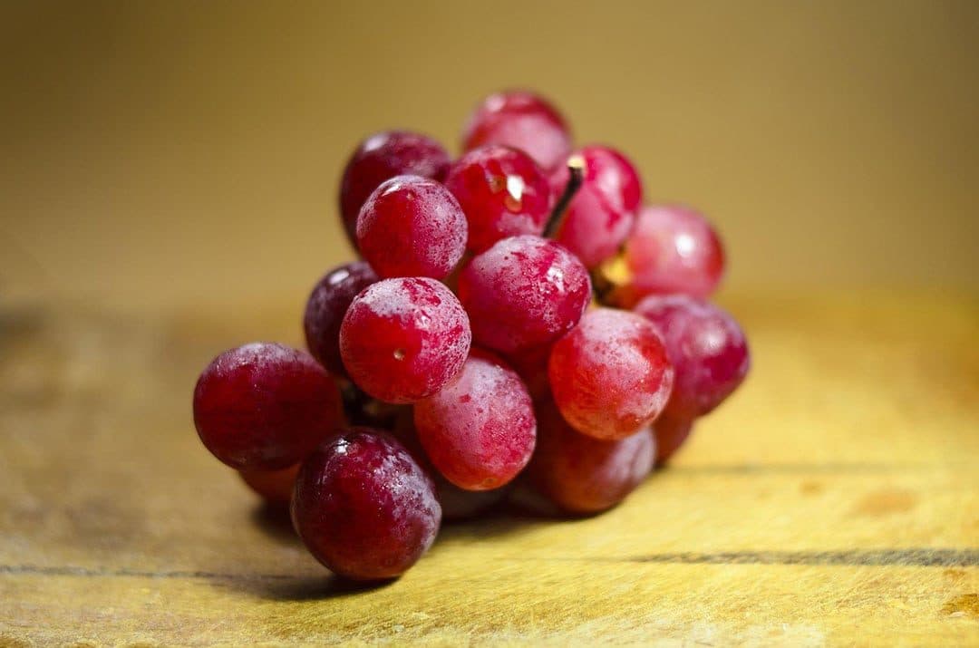 Bunch of red grapes on warm golden wood, soft amber background