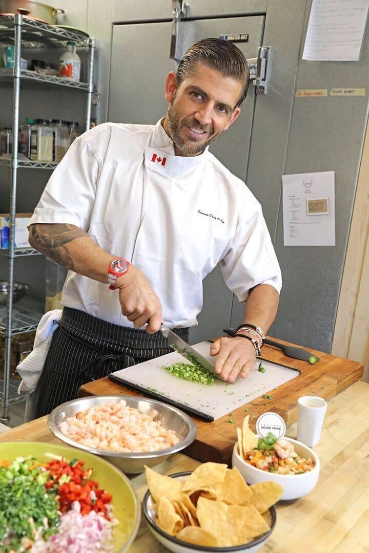 Chef in white jacket dicing at a prep table surrounded by ceviche ingredients and chips