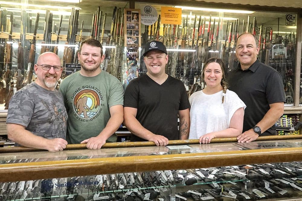 Five family members of Mark Fore & Strike behind a glass display counter with guns on the wall