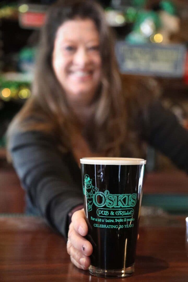 Pub owner presenting a pint of Guinness in an O'Skis glass toward the camera, blurred background