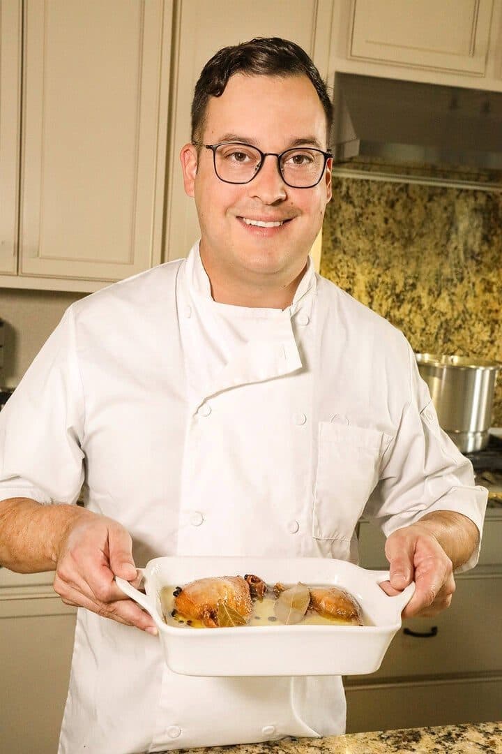 Chef in whites holding a dish of duck confit in a home kitchen