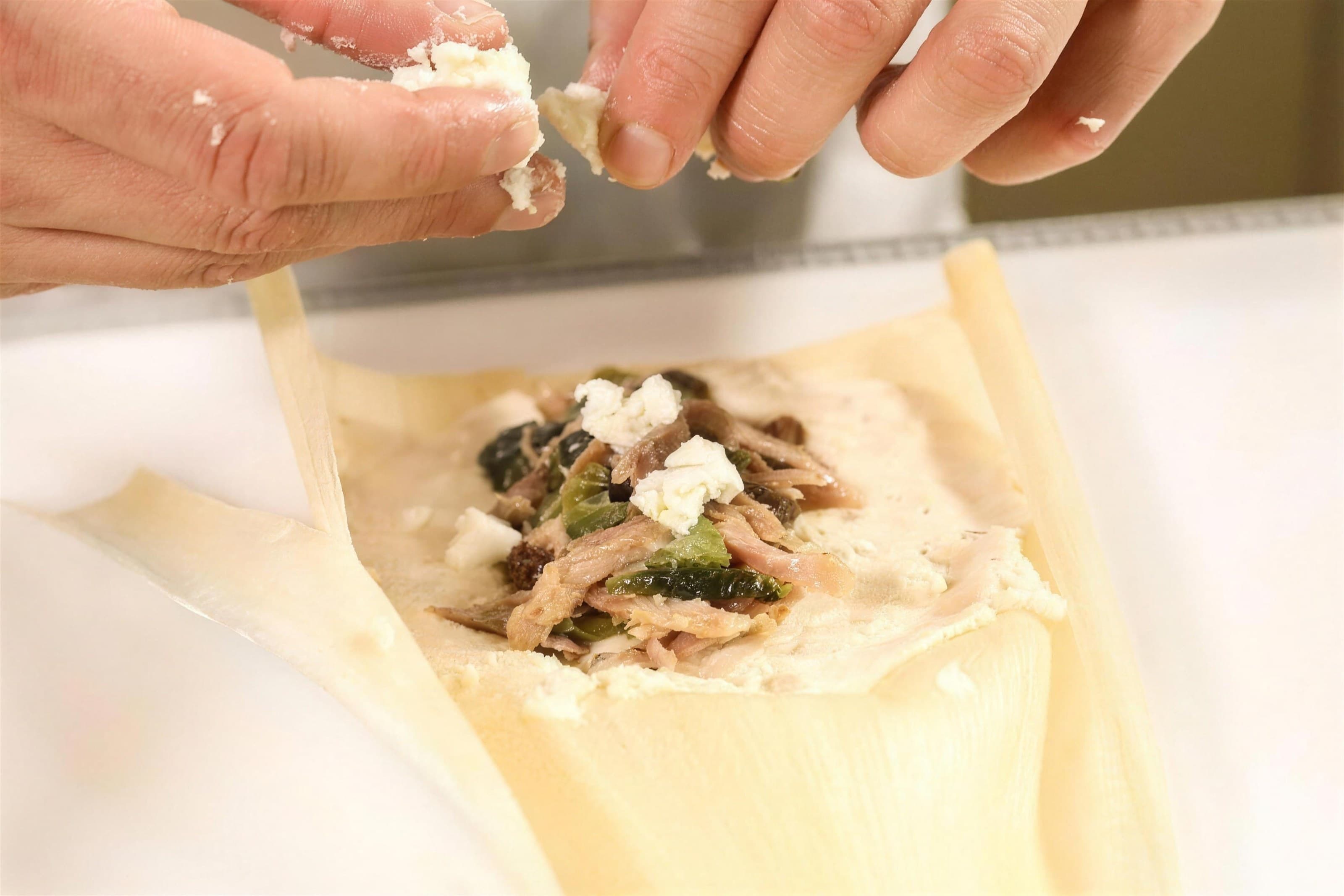 Hands filling a corn husk with masa and shredded duck