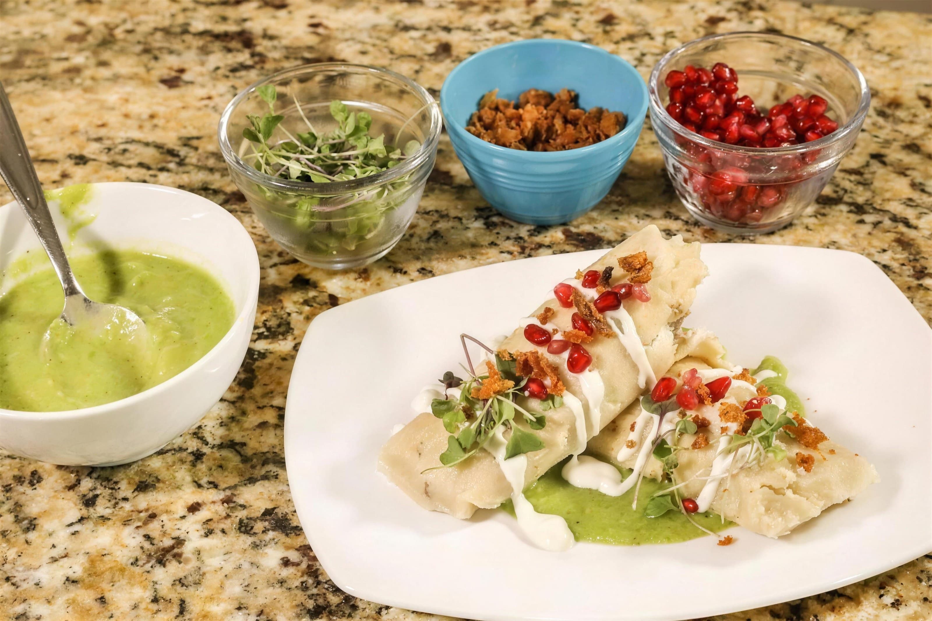 Plated duck tamales with bowls of salsa verde, pomegranate and garnishes