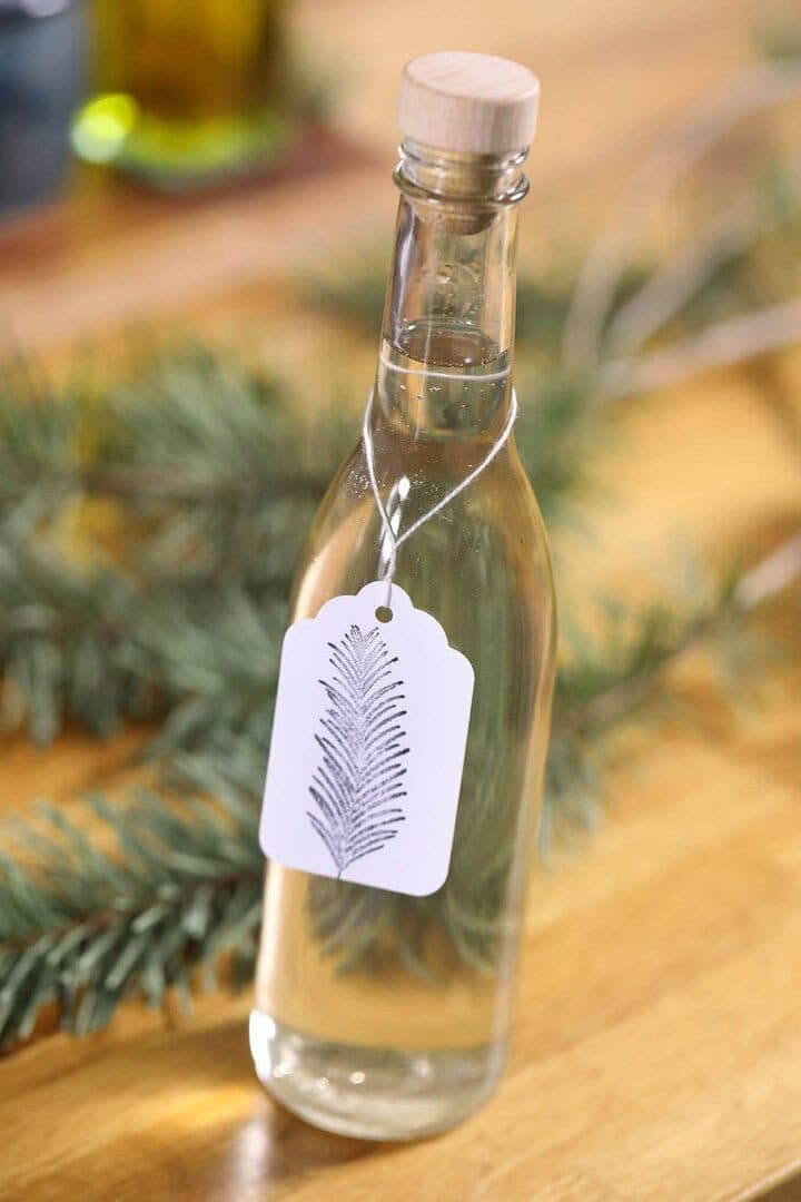 Bottle of Douglas fir simple syrup with a hand-stamped tag on wood among fir boughs