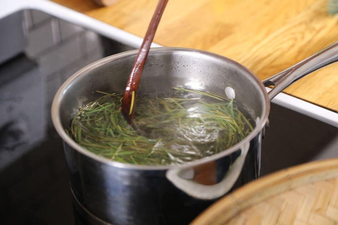 Fir needles steeping in syrup with a wooden spoon in a saucepan