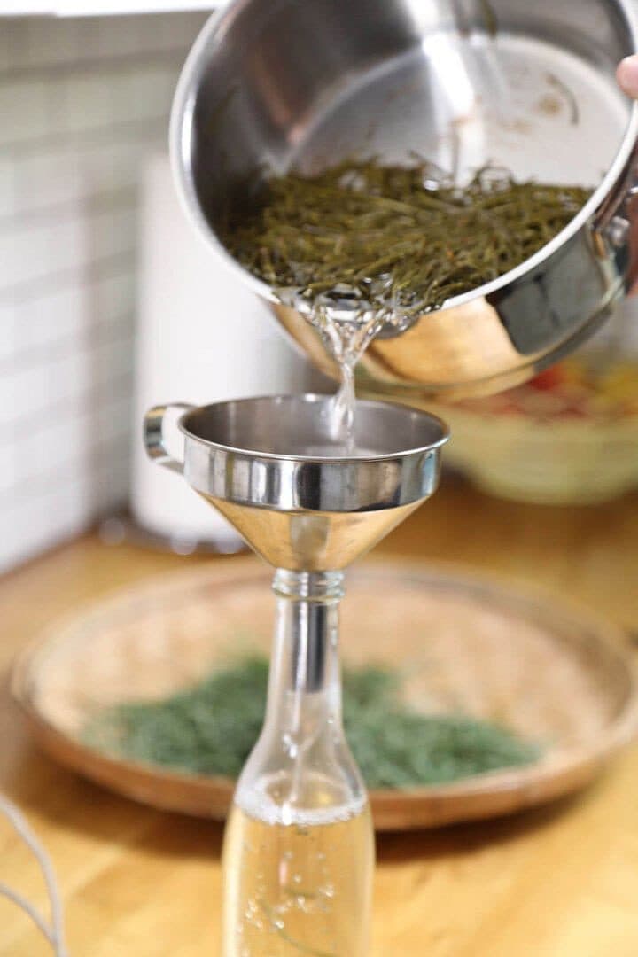 Pouring strained fir syrup through a funnel into a bottle