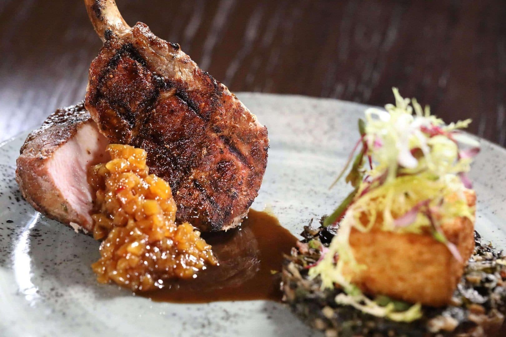 Grilled pork chop with chutney and crispy cake on a gray plate, dark moody