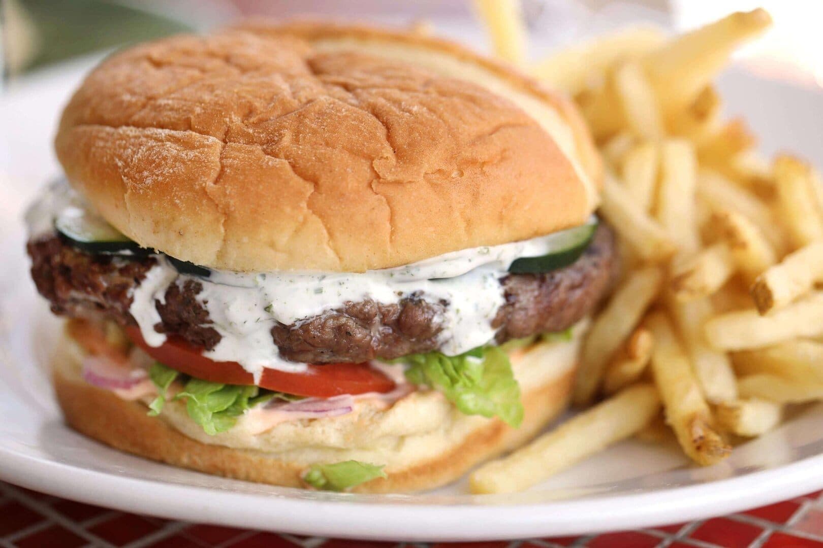Lamb burger with tzatziki and fries on a white plate, red tile table