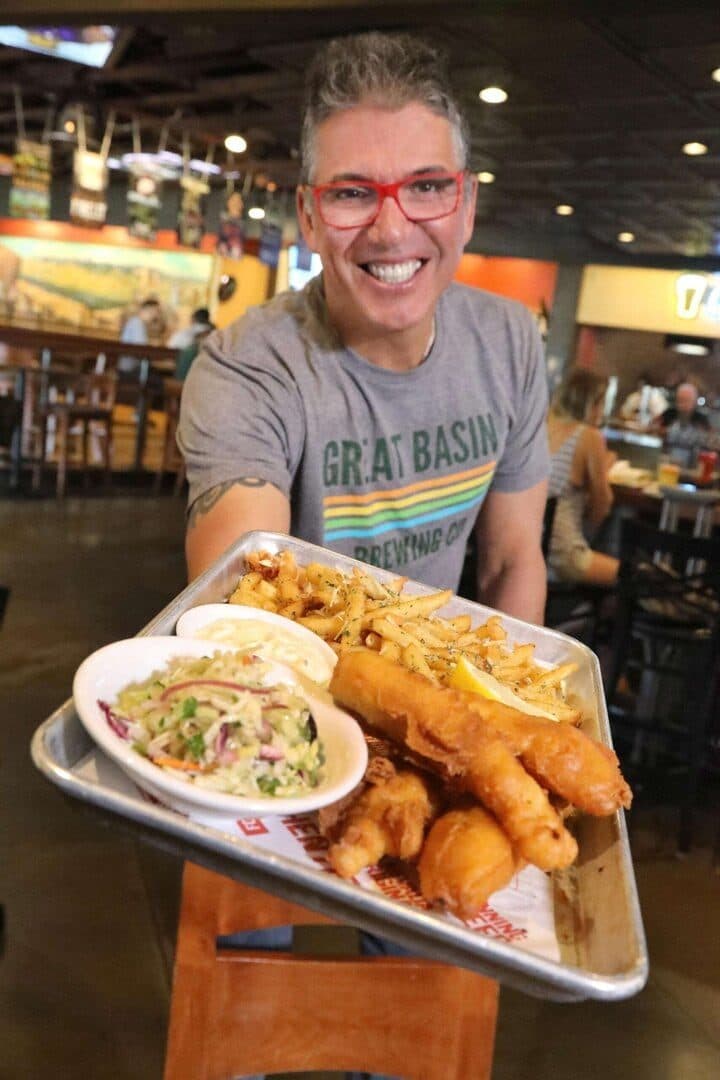 Chef Mark Estee holding a fish-and-chips platter toward camera in a pub