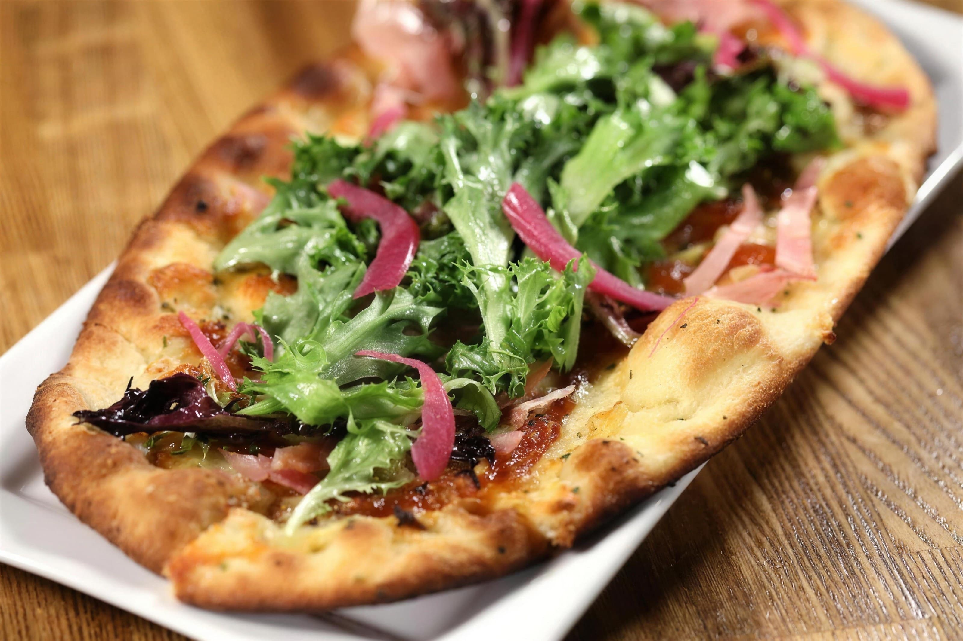 Onion tart flatbread topped with arugula and pickled onion, warm wood