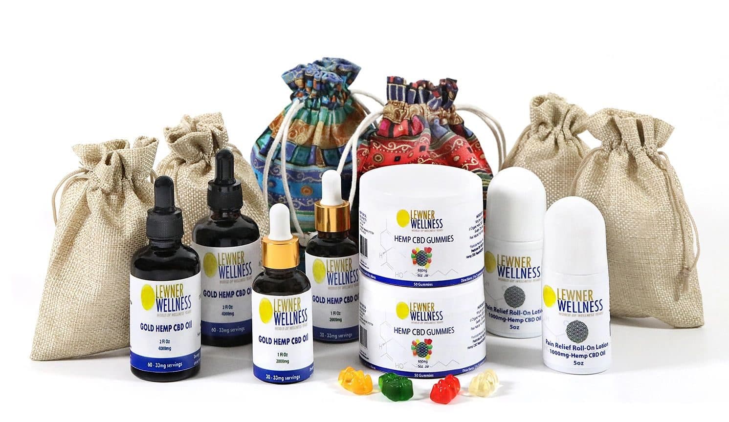Catalog group shot of Lewner Wellness hemp CBD products (oil dropper bottles, gummy jars, roll-on lotion) with burlap and patterned drawstring bags and loose gummy bears; clean white seamless background, even soft light.
